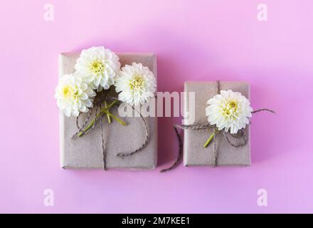 Zwei Geschenkboxen aus grauem Kunsthandwerk mit weißen Dahlienblumen auf pinkfarbenem Hintergrund für die Feiertage. Stockfoto