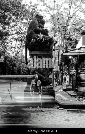 Ein Graustufenfoto eines balinesischen Mannes vor einer riesigen Affenstatue Stockfoto