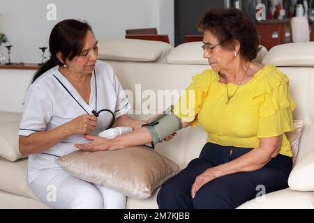 Krankenschwester nimmt Blutdruck einer älteren Frau mit einem digitalen Sphygmomanometer. Hausbesuch zur Überprüfung des Gesundheitszustands eines älteren Patienten. Stockfoto