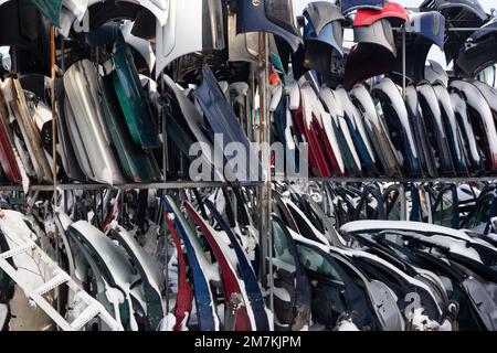 Demontierte Fahrzeuge auf einer Abkippstelle sind als Ersatzteile erhältlich. Ein Stapel Türen und Stoßstangen. Der Handel mit gebrauchten Ersatzteilen ist ein gängiges Geschäft in der Entwicklung Stockfoto