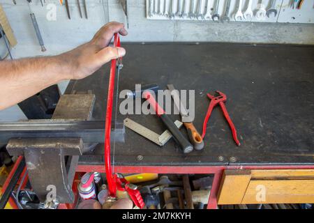 Bild der Hände eines Schmieds, der mit einer Handsäge ein Stück Eisen zerschneidet, das in einem Schraubstock gehalten wird Stockfoto