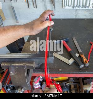 Bild der Hände eines Schmieds, der mit einer Handsäge ein Stück Eisen zerschneidet, das in einem Schraubstock gehalten wird Stockfoto