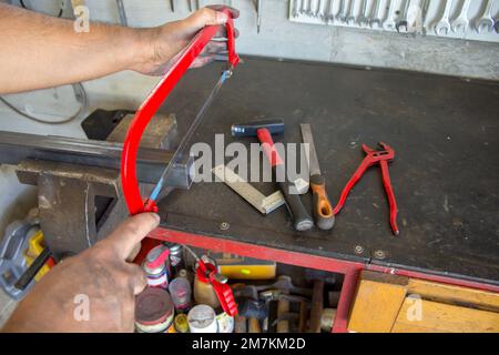 Bild der Hände eines Schmieds, der mit einer Handsäge ein Stück Eisen zerschneidet, das in einem Schraubstock gehalten wird Stockfoto