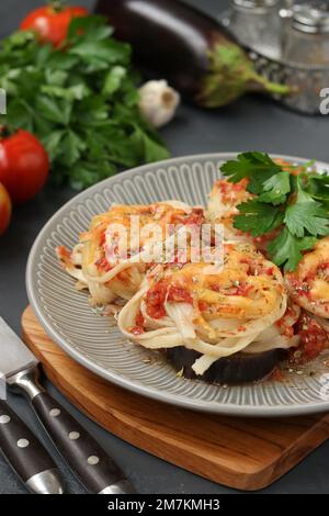 Spaghetti mit Auberginen, Tomaten und Käse auf einer grauen Platte auf Holzbrett. Vegetarisches Essen Stockfoto