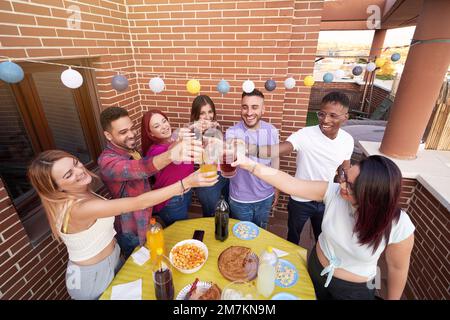 Eine Gruppe glücklicher Freunde, die mit Getränken anstoßen, während sie draußen auf der Terrasse feiern. Freundschaftskonzept. Stockfoto