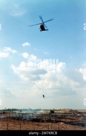 DF-SD-03-17788. [Complete] Scene Caption: Während der Kaman HH-43F Huskie (Pedro) schwebt, wird DER FLIEGER First Class (A1C) William Hart Pitsenbarger, USAF, Pararescue Crew Member, Detachment 6, 38. Aerospace Rescue and Recovery Squadron (ARRS) entfernt, während er einen verwundeten Soldaten der Republik Vietnam (ARVN) aus dem brennenden Minenfeld hält. Der Soldat verlor einen Fuß, als er auf eine Landmine trat. Niemand konnte herausfinden, wie man den verwundeten Soldaten entführt, ohne die Minen auszulöschen. A1c Pitsenbarger sagte: „Kein Problem, lass mich einfach auf den Eindringkörper runter, ich werde den Kerl überqueren, ihn hochheben und t Stockfoto