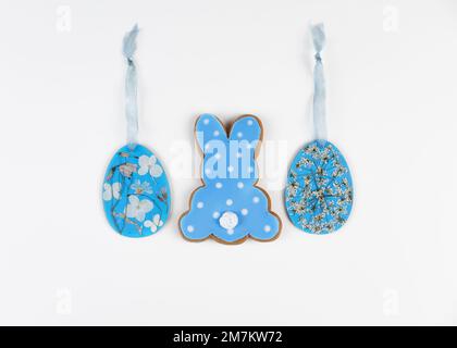 Blaues Lebkuchen in Form von Kaninchen und zwei Sperrholzrohlinge in Form von Ostereiern, dekoriert mit gepressten getrockneten Blumen. Trendige Ostereinrichtung. Stockfoto