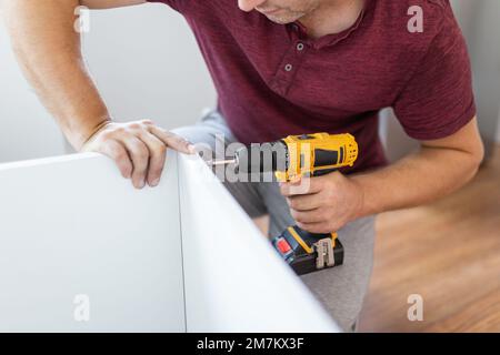 Nahaufnahme eines Mannes, der während der Installation von hölzernen Küchenregalen einen elektrischen Akkuschrauber hält Stockfoto