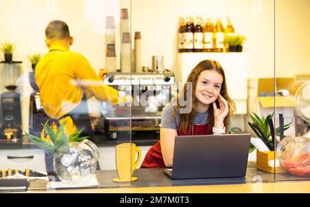 Gruppe von Barista Café oder Barkeeper, die im Café arbeiten. Baristas Frau, die im Café arbeitet und einen Laptop-Computer tippt, ist glücklich und lächelt. Klein Stockfoto