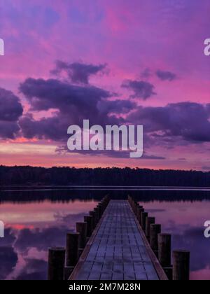 Eine vertikale Aufnahme eines faszinierenden violetten Sonnenuntergangs über dem Seeufer mit einem Pier Stockfoto