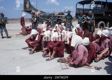 Vietcong-Kriegsgefangene sitzen unter den wachsamen Augen der südvietnamesischen Militärpolizei auf der Rampe des Luftwaffenstützpunktes Tan Son Nhut. Die Kriegsgefangenen wurden in DEN 6X6-Lastwagen im Hintergrund zum Luftwaffenstützpunkt gebracht und werden mit dem C-123-Transportflugzeug nach Loc Ninh, Südvietnam, für den Gefangenenaustausch zwischen den Militärs der Vereinigten Staaten/Südvietnam und Nordvietnam/Vietcong geflogen. Subjekt Operation/Serie: HOMECOMING-Basis: Saigon-Land: Südvietnam Stockfoto