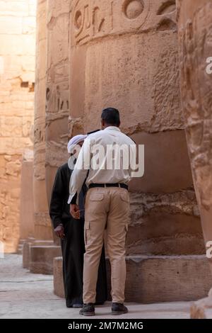 LUXOR, ÄGYPTEN - 27. Dez. 2022. Der Wachmann spricht mit einem eisigen Mann zwischen den antiken Ruinen des Karnak-Tempels in einer Reihe von Säulen mit geschnitzter Kiste Stockfoto