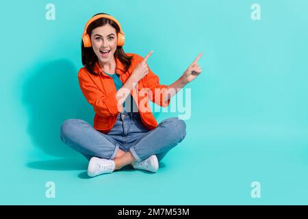 Foto in voller Länge mit niedlichem, beeindruckendem Hemd in Mädchenoptik, das Musik auf leeren Raum zeigt, isolierter türkisfarbener Hintergrund Stockfoto