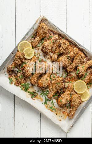 Sesamhähnchen mariniert mit Harissa-Paste auf einem Backblech isoliert auf weißem Holzhintergrund mit Platz für Text Stockfoto