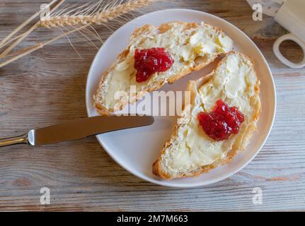 Croissant mit Butter und Erdbeermarmelade auf einem Teller zum Frühstück Stockfoto