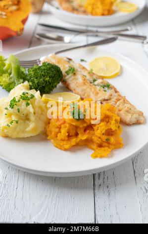 Fischfilet mit Kartoffelpüree und rotem Kuri-Kürbispüree. Serviert mit Brokkoli auf einem Teller Stockfoto