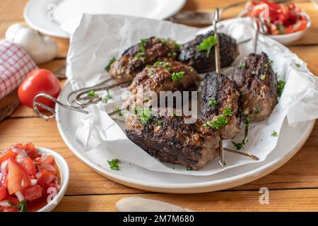 Hackfleischspieß mit Rinderhack und Tomatensalat auf einem Holztisch Stockfoto