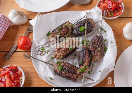 Scharfes Rinderhack, Cevapcici Spieße mit Tomatensalat auf einem Holztisch. Draufsicht Stockfoto