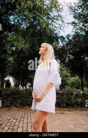 Glückliche schwangere Frau in blauem Kleid im Garten an Sommertagen Stockfoto