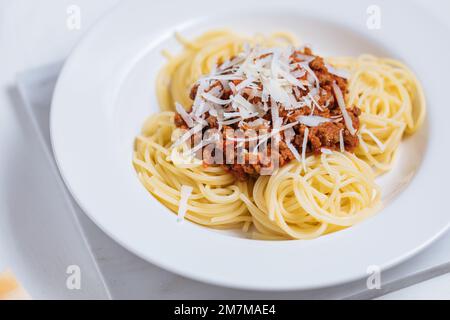 Draufsicht auf bolognesische Spaghetti mit Parmesankäse auf weißem Teller. Einfacher weißer Hintergrund und Dekoration. Traditionelles italienisches Gericht, Mediterr Stockfoto