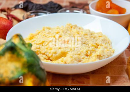 Nahaufnahme von Kürbisbrei mit Hirse, serviert in einer weißen Schüssel, selektiver Fokus, horizontaler Schuss. Stockfoto