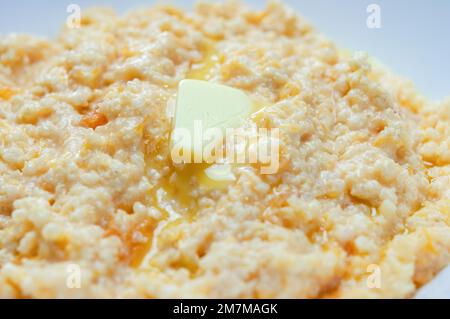 Nahaufnahme von Kürbisbrei mit Hirse und Butter, serviert in einer weißen Schüssel, selektiver Fokus, horizontaler Schuss. Stockfoto