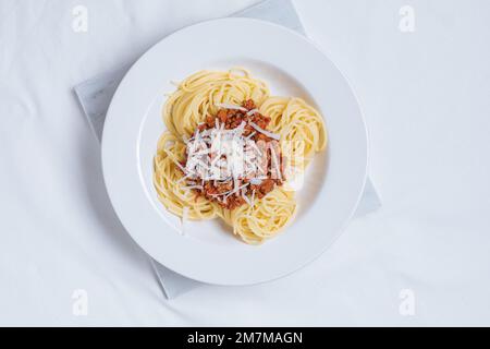 Draufsicht auf bolognesische Spaghetti mit Parmesankäse auf weißem Teller. Einfacher weißer Hintergrund und Dekoration. Traditionelles italienisches Gericht, Mediterr Stockfoto