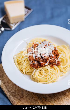 Bolognese-Spaghetti mit Parmesankäse auf weißem Teller. Einfacher blauer Hintergrund und Dekoration. Traditionelles italienisches Gericht, mediterrane Küche Stockfoto