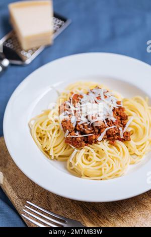 Bolognese-Spaghetti mit Parmesankäse auf weißem Teller. Einfacher blauer Hintergrund und Dekoration. Traditionelles italienisches Gericht, mediterrane Küche Stockfoto