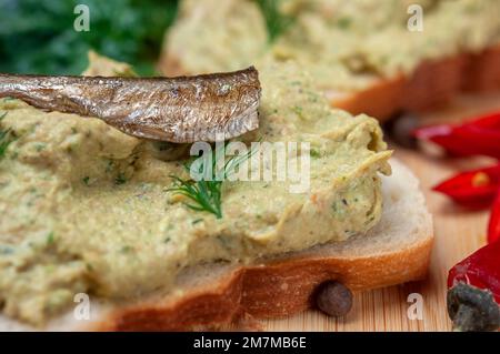 Sandwich mit Pastete und Sprotten. Sprottenpastete mit Spinat und Pfeffer. Sprotte in Öl, dänische Küche. Hintergrund zu Lebensmittelrezepten. Sandwich mit geräucherter Sprotte. Stockfoto