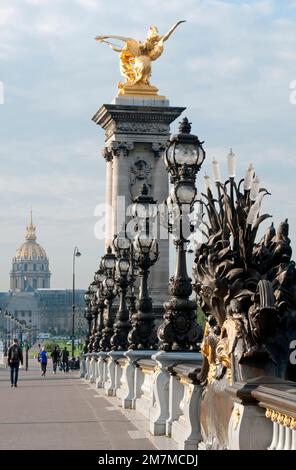 Fußgänger gehen auf der prunkvollen Brücke Pont Alexandre III in Paris, mit dem Wahrzeichen Dôme des Invalides im Hintergrund. Stockfoto