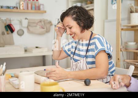 Eine lächelnde Frau, die in einem Töpferkurs Kunsthandwerk herstellt. Handwerk, Kunst und Hobbys. Stockfoto