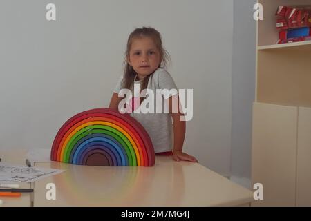 Ein wunderschönes kleines Mädchen, das mit farbenfrohem Holzspielzeug Regenbogen im Kinderzimmer spielt. Unschärfe-Effekt Stockfoto