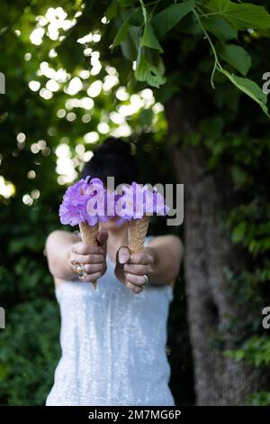 Dunkelhaarige Frau hält zwei Eiskegel mit Blumen vor dem Gesicht Stockfoto