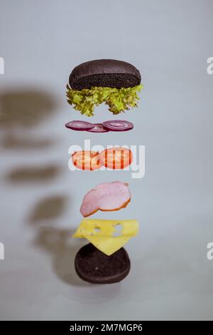 Fliegender Hamburger, unterteilt in Tomaten, Zwiebeln, Käse, Kohl, Brötchen, Schinken Stockfoto