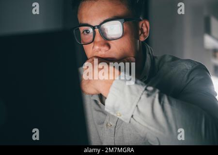 Nahaufnahme und Porträt eines jungen Teenagers, der abends zu Hause auf dem Tisch lernt und arbeitet, indem er einen lächelnden Laptop benutzt und Spaß bei den Hausaufgaben hat. Licht des Bildschirms auf dem Gesicht. Stockfoto