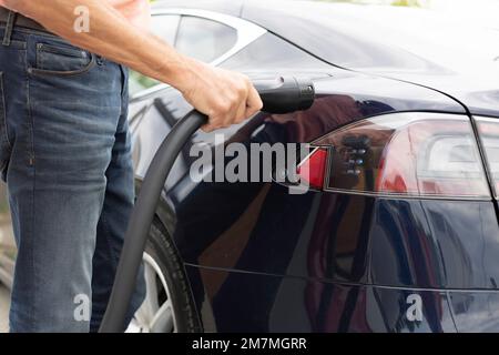 Mann an der Ladestation verbindet seinen Tesla mit dem Ladekabel Stockfoto