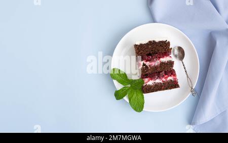 Ein Stück Schokoladenschwammkuchen mit weißer Beerenfüllplatte und pastellblauem Hintergrund. Süßes Dessert Stockfoto