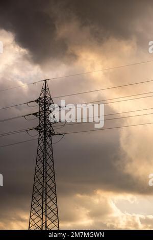 Hochspannungskabel in einem dramatischen bewölkten Sonnenuntergang Stockfoto
