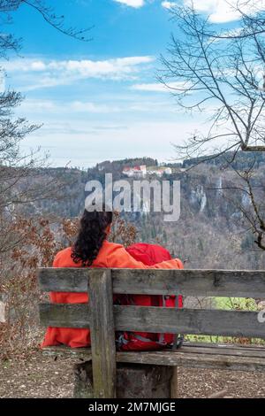 Europa, Deutschland, Süddeutschland, Baden-Württemberg, Donautal, Sigmaringen, Beuron, Wanderer sitzt auf einer Holzbank und genießt den Blick auf das Schloss Wildenstein und das Donautal Stockfoto