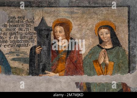 Die Heiligen Barbara (links) und Margherita oder Margaret von Cortona, dargestellt in beschädigtem Renaissance-Fresko, gemalt 1512, an der Westfront der entsezten Cappella di San Grato (Kapelle St. Gratus) in der Via Jean-Baptiste De Tillier im historischen Zentrum von Aosta, Regionale Hauptstadt des Aostatals im Nordwesten Italiens. Die heilige Barbara hat einen Turm mit drei Fenstern. Der Turm symbolisiert Barbaras Gefangenschaft durch ihren Vater. Die drei Fenster, die sie in ihr Gefängnis einführen ließ, symbolisieren die Heilige Dreifaltigkeit. Stockfoto