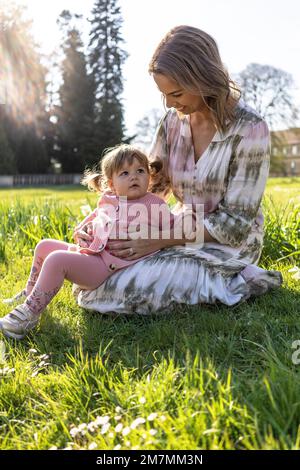 Europa, Deutschland, Baden-Württemberg, Stuttgart, Schloss Hohenheim, Mutter sitzt mit der kleinen Tochter auf einer Wiese vor dem Schloss Hohenheim Stockfoto