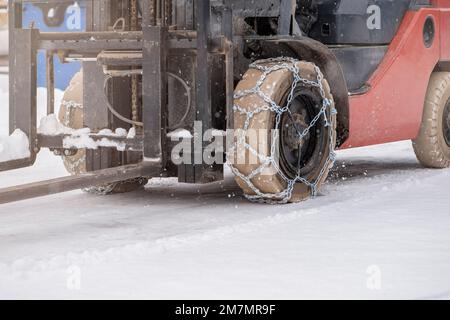 Traktorrad mit Kette. Traktor oder Lader auf einer rutschigen, verschneiten Straße. Lader fahren mit rutschfesten Ketten auf Schnee. Stockfoto
