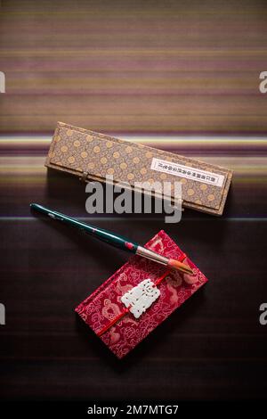 Stille Leben mit Pinsel, asiatische Box und ein rotes Buch auf gestreiftem Hintergrund Stockfoto