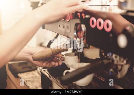 Nahaufnahme eines Baristas, der die Kaffeetasse mit der Kaffeemaschine in der Bar hält Stockfoto
