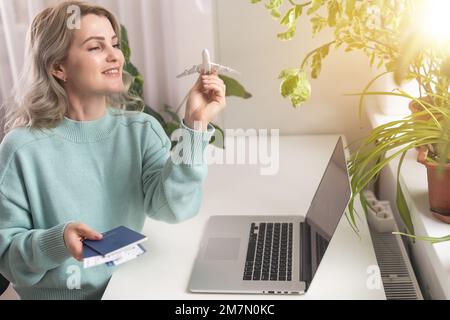 Nahaufnahme von Frauenhänden, die ein Modellflugzeug halten und einen Laptop benutzen, Flug online buchen und Reservierungskonzept. Stockfoto