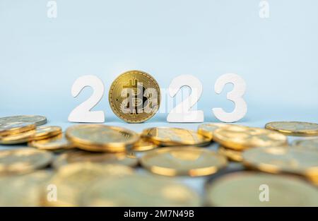 Bitcoin 2023-Preisprognose. BTC-Münze neben Kryptowährungs-Token und Jahreszahlen auf blauem Hintergrund. Nahaufnahme, Soft Focus. Stockfoto