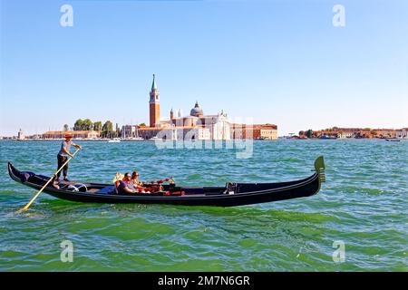 Mann und Frau ließen sich von einem Gondoliere auf dem Canal Grande in Venedig in einer Gondel fahren. Dahinter, direkt am Canale Grande, befindet sich die barocke Kirche Santa Maria della Salute, erbaut von 1631 von Baldassare Longhena, 1687 geweiht. Ebenfalls sichtbar ist der Glockenturm Campanile di San Marco, Stockfoto