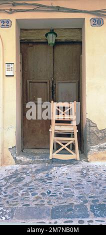 Zwei Holzstühle sind vor der alten Eingangstür in Cefalu, Sizilien, gestapelt Stockfoto