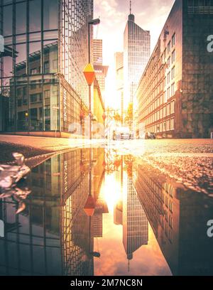 Blick auf eine Schlucht am Morgen. Mit Sonnenlicht und Reflexion in einer Pfütze auf der Straße in Frankfurt am Main, Hessen Stockfoto